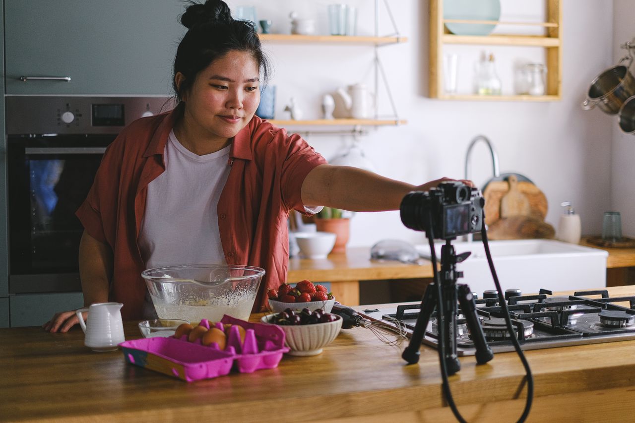 Home A woman films a cooking vlog in a cozy and modern kitchen with fresh ingredients.